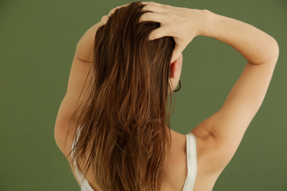 Frau massiert natürlich gepflegtes, langes braunes Haar vor grünem Hintergrund – Anwendung von Rosmarinöl gegen Haarausfall und zur Beruhigung der Kopfhaut